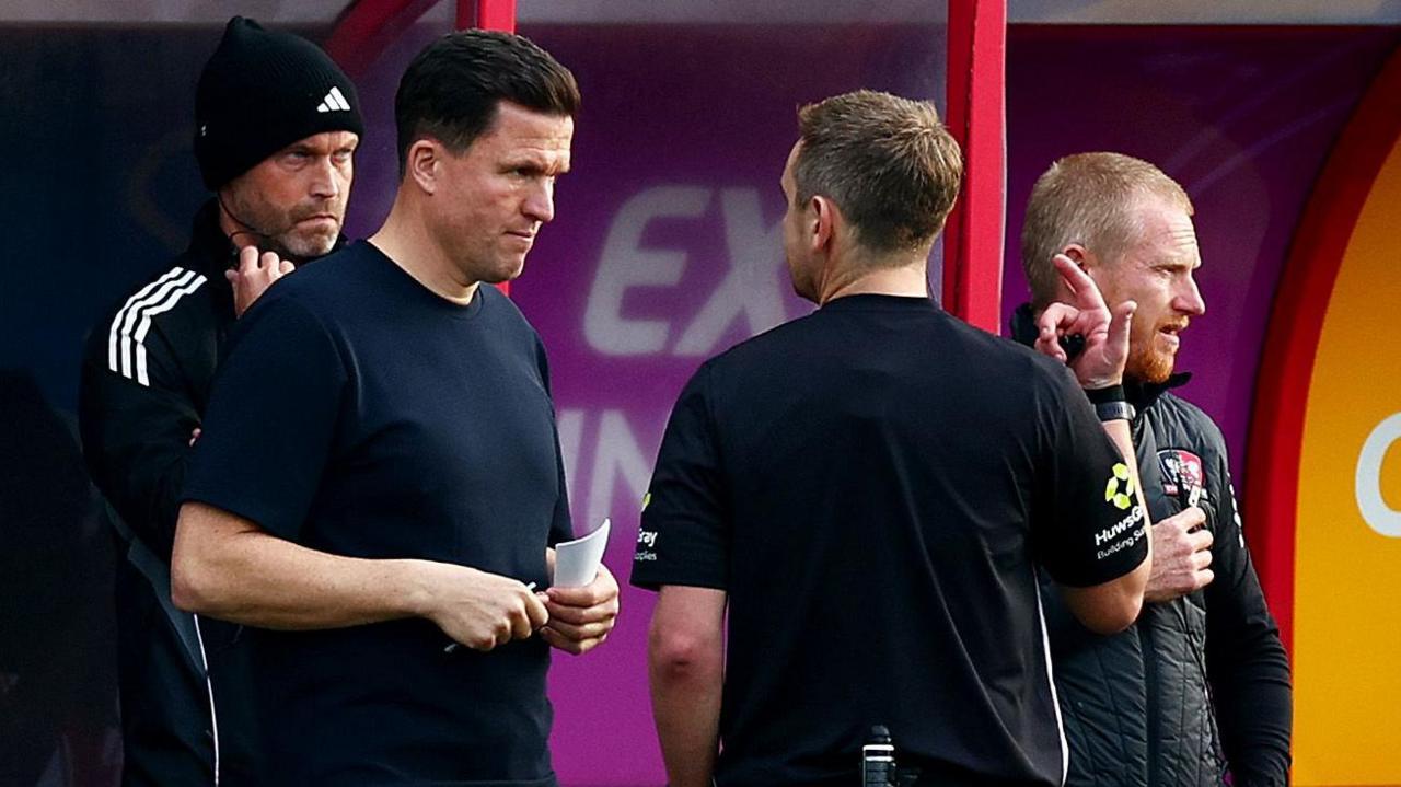 Exeter City manager Gary Caldwell (left) talks to referee James Durkin about the stoppage following an allegation of racist abuse