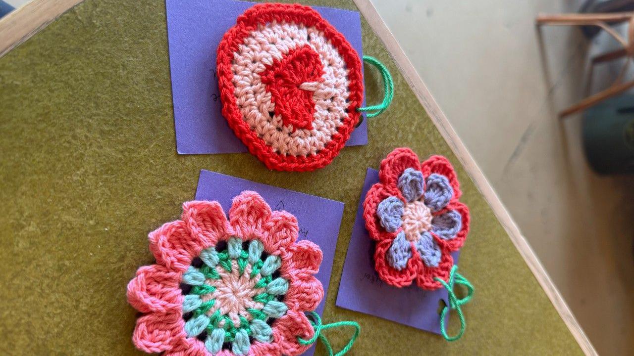 Crochet flowers on a table with pieces of purple card attached to them