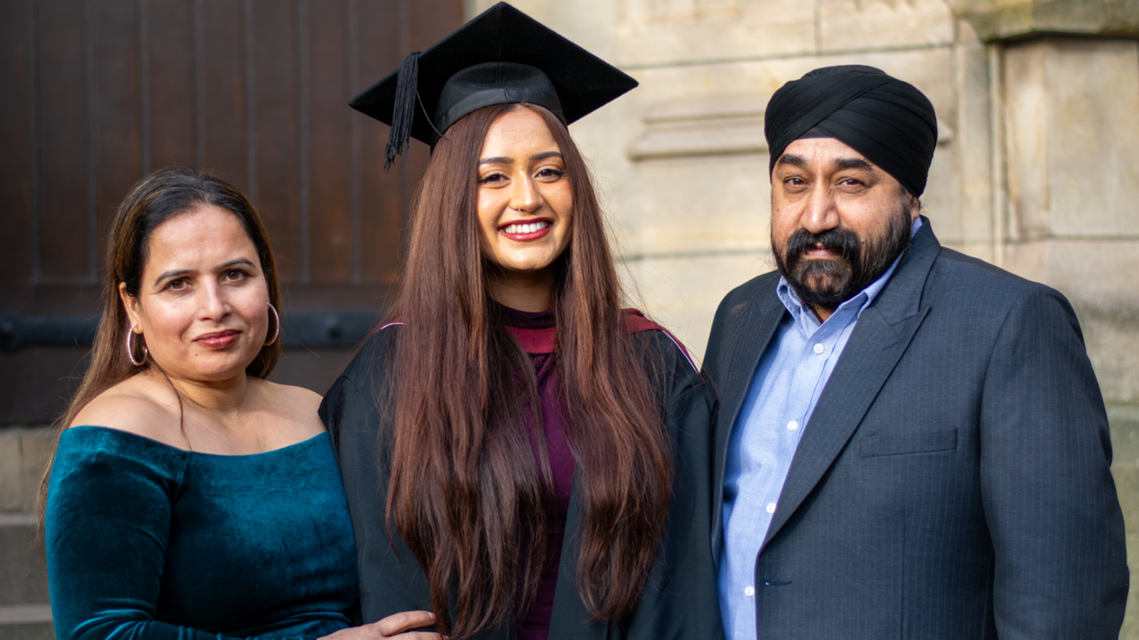 Gurvin Chopra is standing between her parents Jaspal and Waryam Chopra. Gurvin is wearing a Bristol University graduation robe and hat. Her father is wearing a suit and her mother is wearing a turqouise dress. Gurvin is smiling.