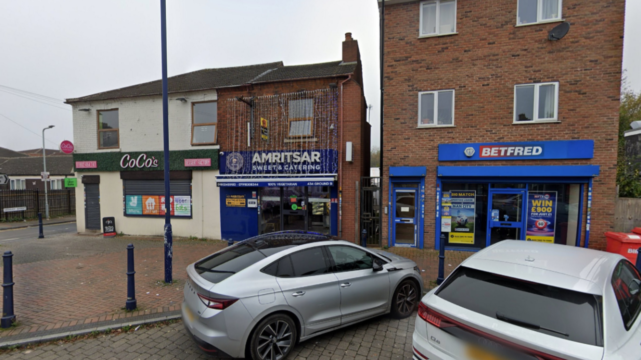The shop is pictured in between two others and has blue sign outside with decorative lights cascading from near the roof down to above the front entrance