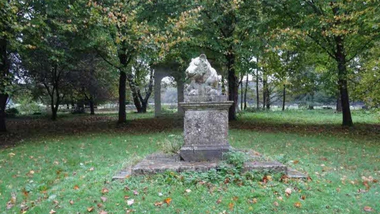 Stone statue of a lioness on a plinth, surrounded by trees