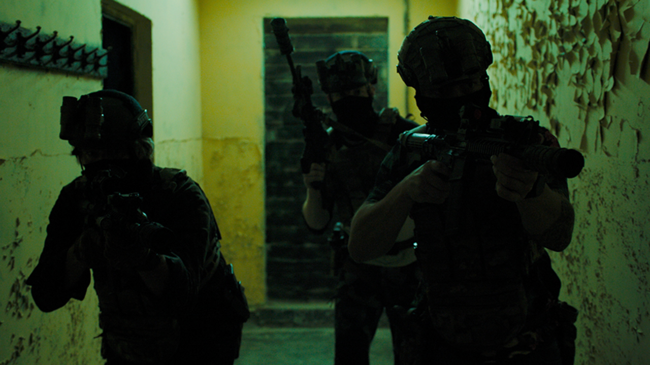 Three men in military gear and guns walk down an unlit corridor as part of a film still from Sunray. 