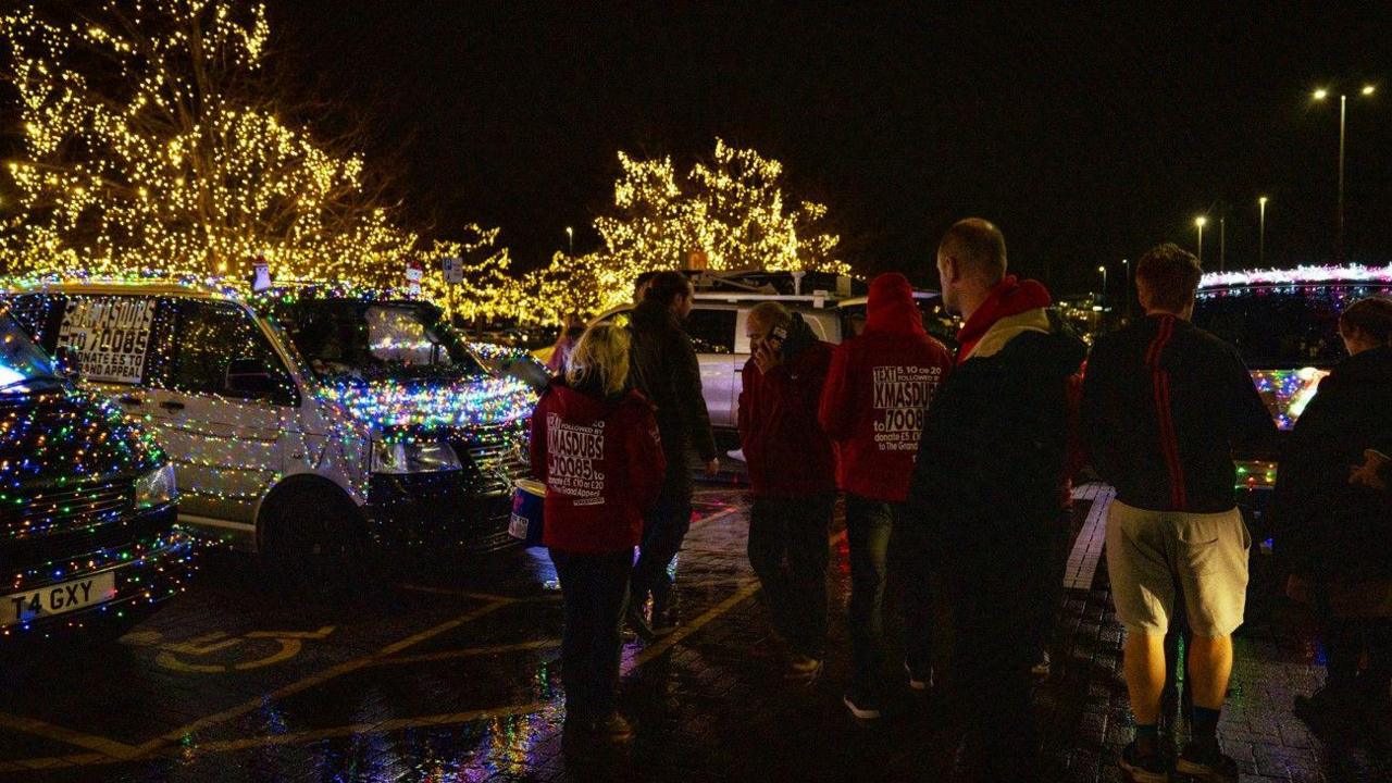 A group of people looking at the lit-up vans outside at night