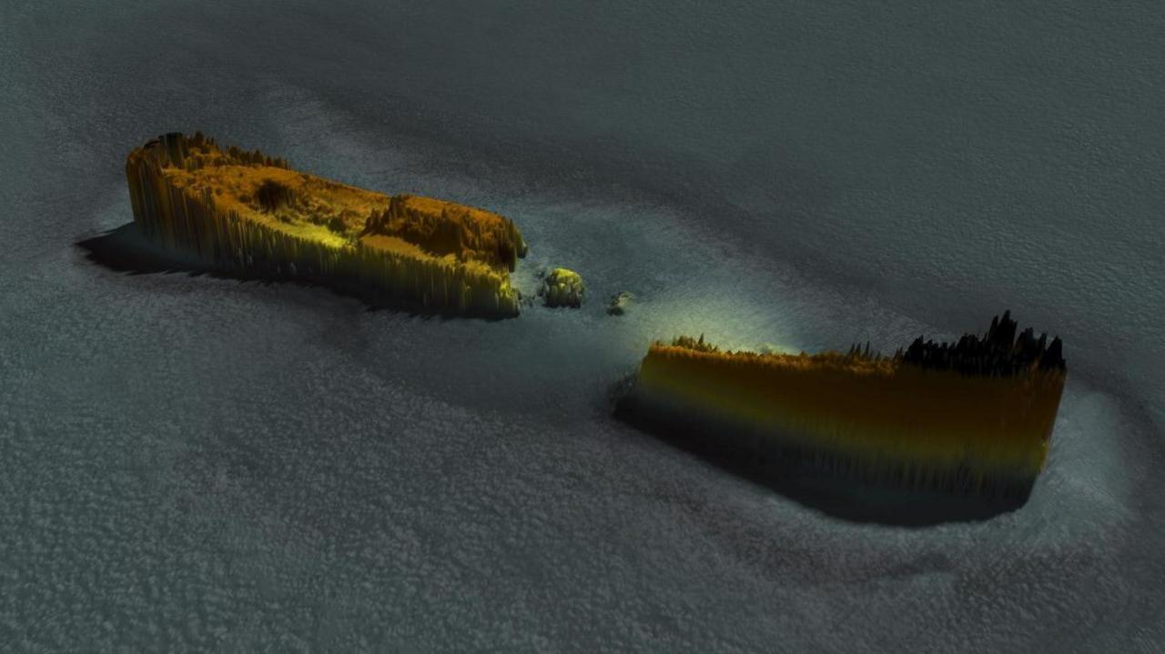 A graphic produced after the team used a multibeam sonar to scan the sea bed and shipwreck. The wreck is coloured based on height out of the seabed. It is jagged and bits of the ship are missing. 