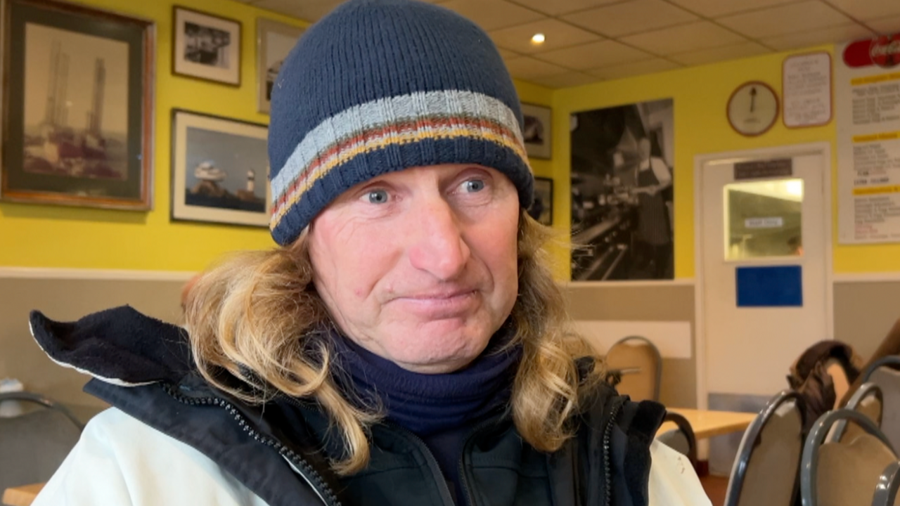 Man in beanie hat and long hair sits in a cafe with nautical pictures on the yellow walls