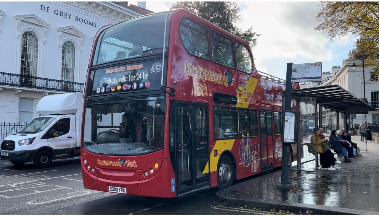 A bright red double-decker bus waits at a bus stop in York.