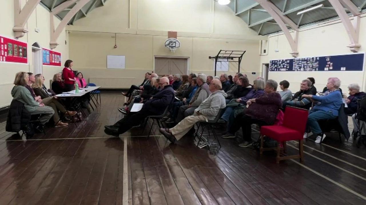 Patients in a hall listening to NHS bosses