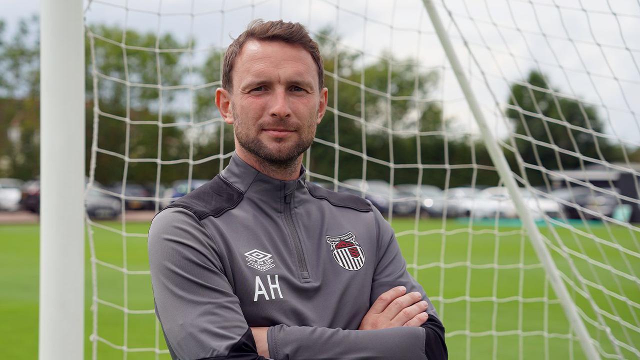 Alex Hughes posing for a picture while stood in a goal wearing a Grimsby Town tracksuit