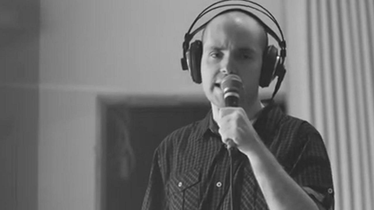 A man with a bald head, wears a headphone set and sings into the microphone in a studio 