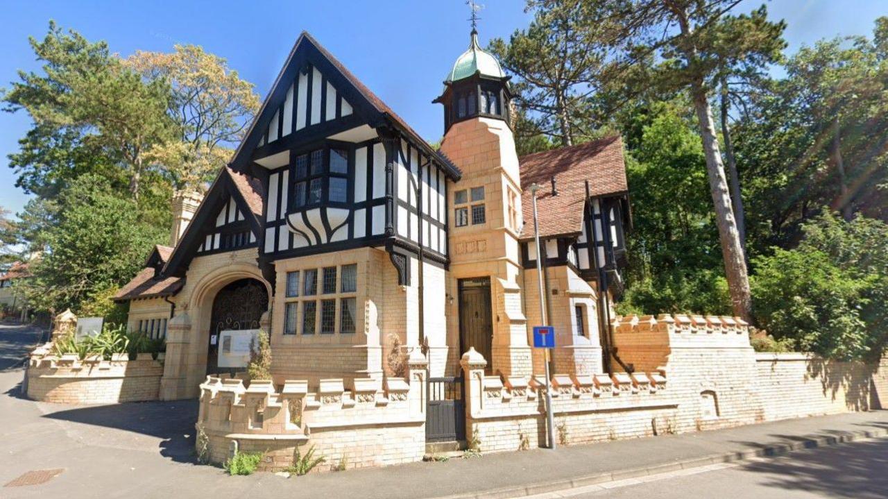 The Grade II listed St Mary's Lodge on the corner of a road junction. The ground floor exterior and the wall of the site by the pavement are yellow, while the outside of the upper floors is partially white and black in colour.