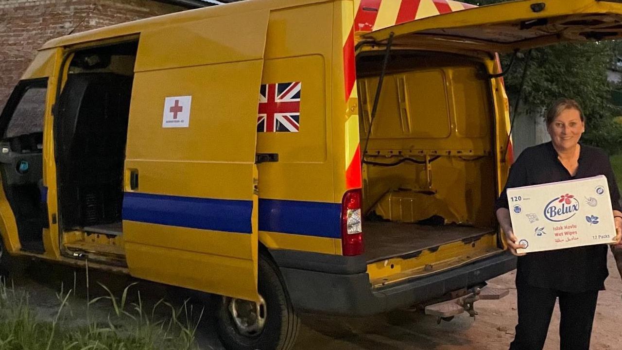 Karen Watt carrying a box next to a large yellow van with the Union Jack flag on.
