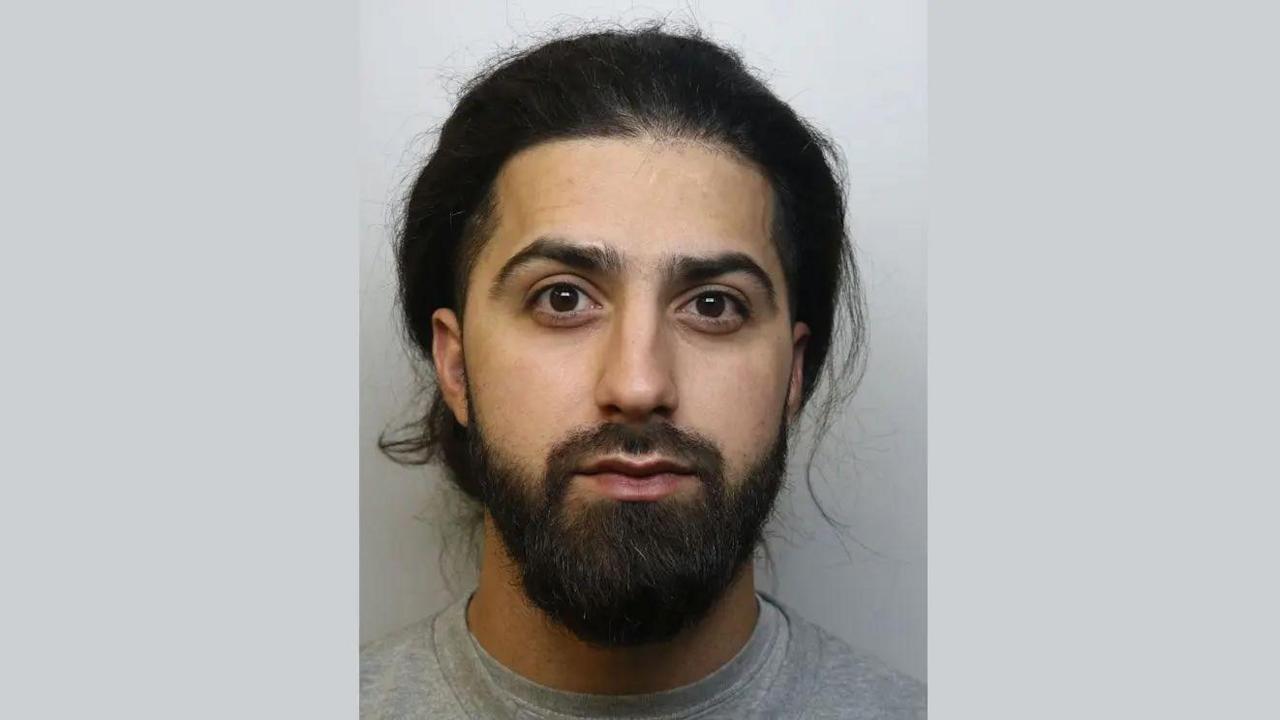 Mugshot of Jegir Asaad. He has long dark hair which is tied back and dark facial hair. He is wearing a grey top and is pictured against a plain background. He is looking directly at the camera with a blank expression.