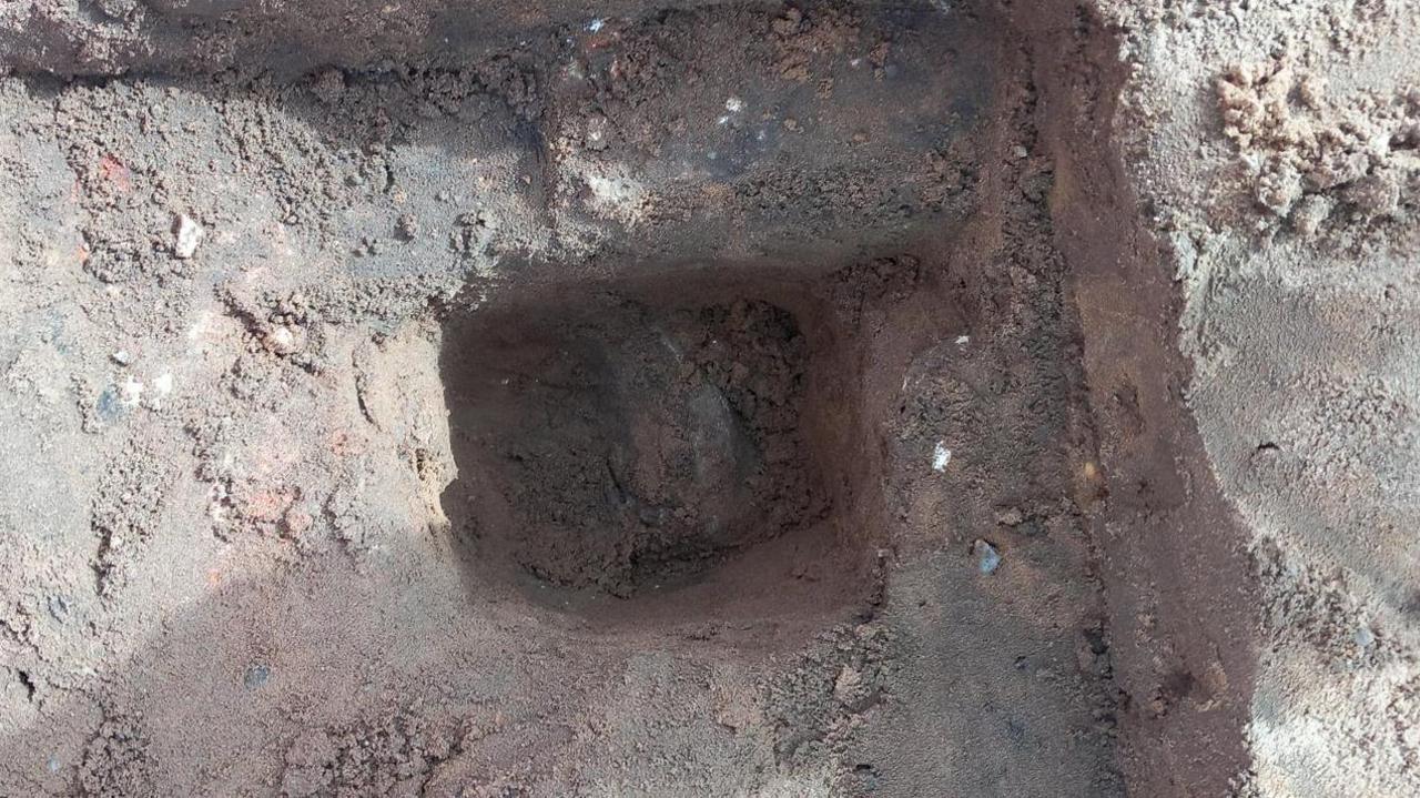 An excavated section of the ground shows a deep well where the bundle of coins is slowly being unearthed by archaeologists. 