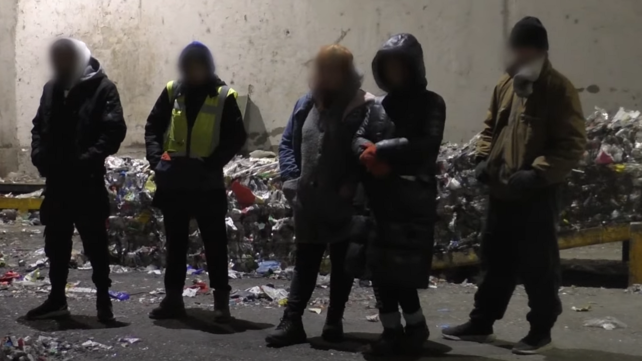 A screengrab from a police video shows some of the men and women arrested in the operation to break up a human trafficking ring. They are standing outside by a rubbish heap, wearing coats, hats and gloves. Their faces are blurred.