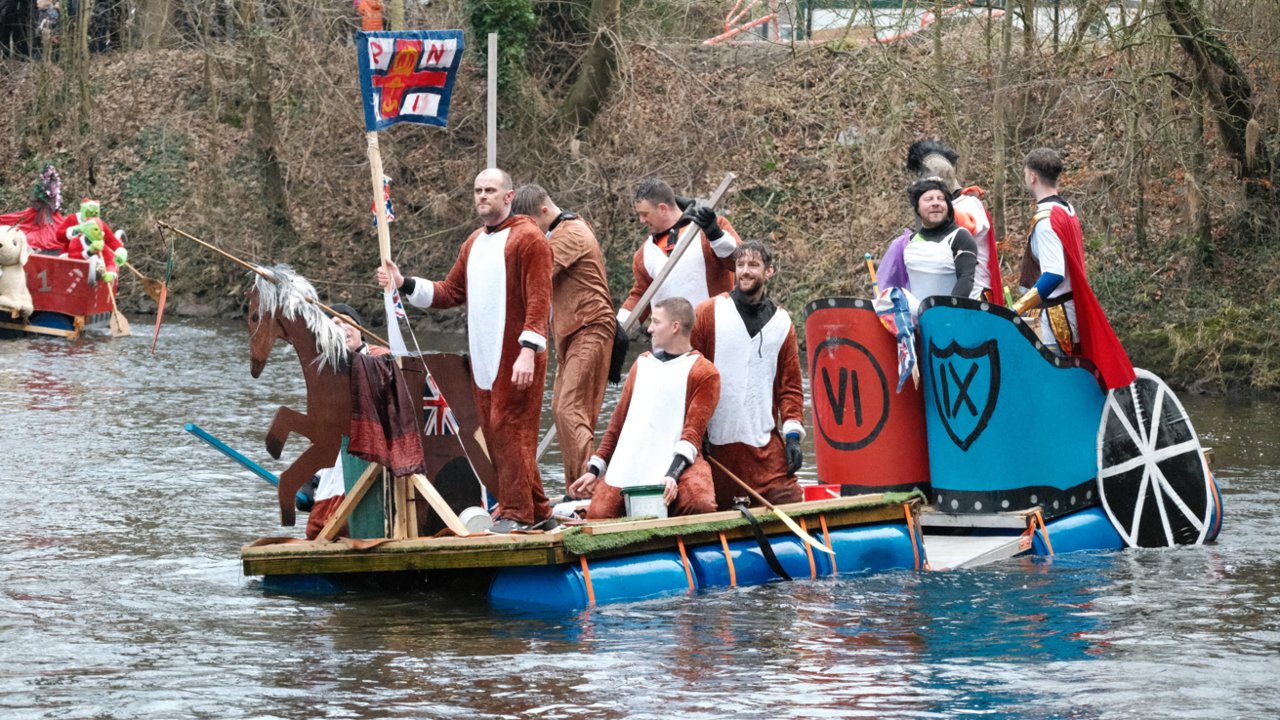 A custom-made raft on a river with men dressed in horse onesies and knight costumes on top with oars.