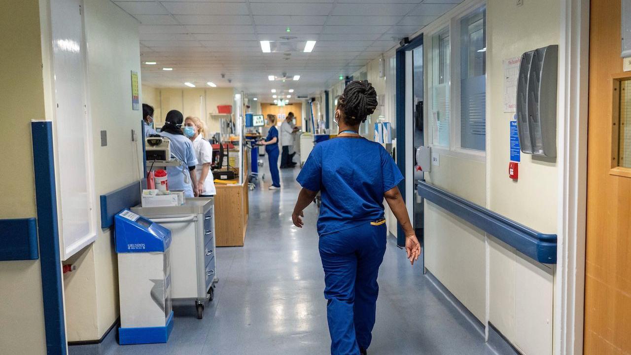 A nurse wears blue scrubs as she walks through a hospital corridor.
