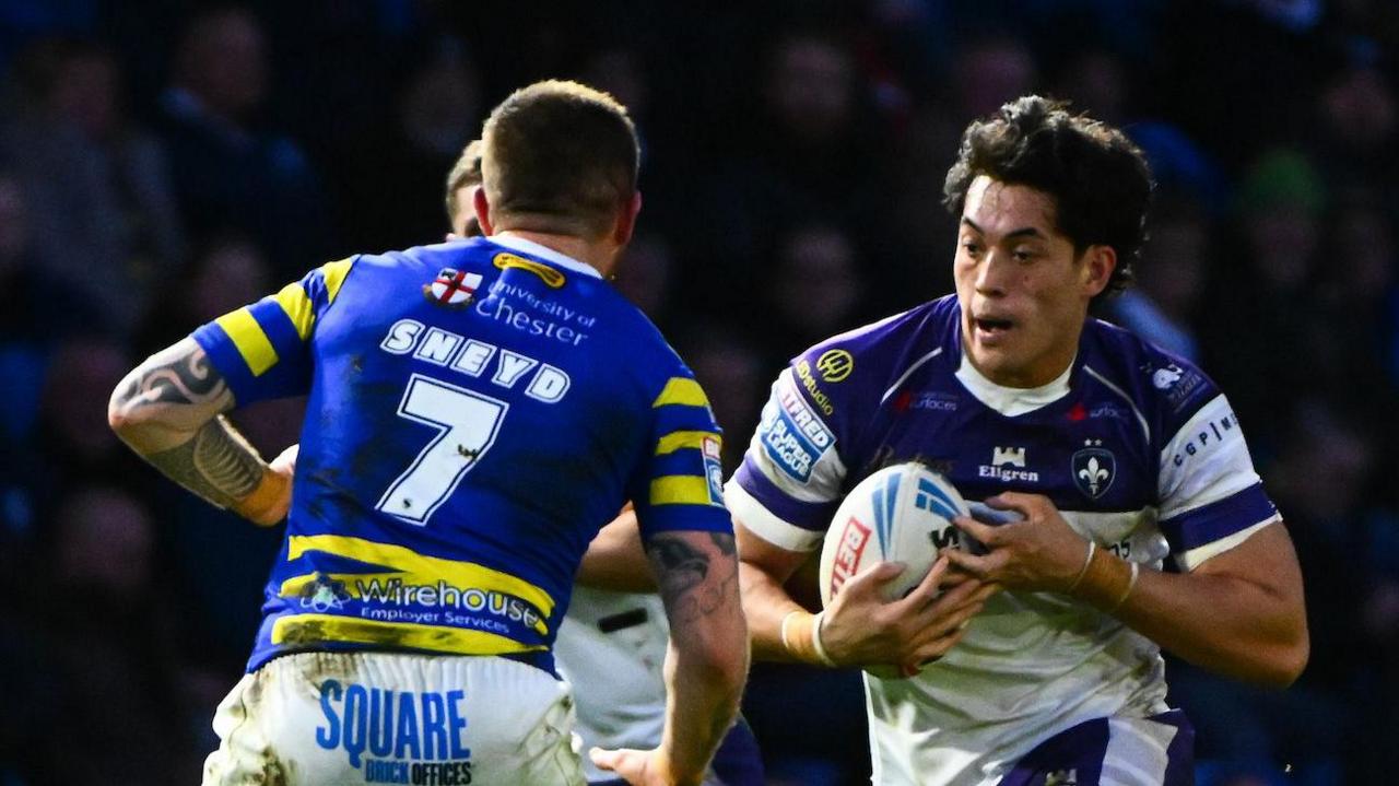 Wakefield's Isaiah Vagana, wearing a white and blue shirt, runs at Warrington's Marc Sneyd