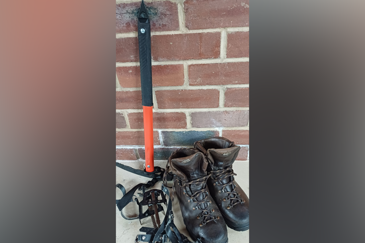 Mountain rescue equipment is laid out. A pair of crampons, an ice axe and a pair of boots. 