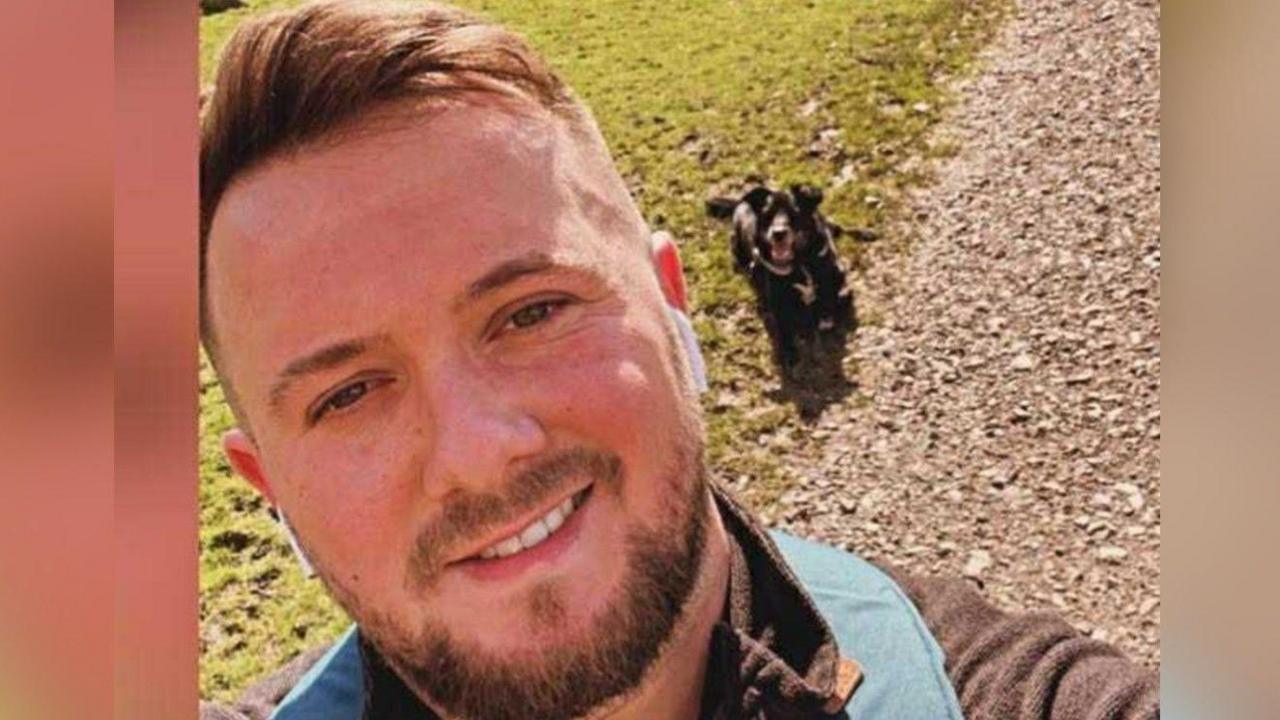 Nathan Clarkson, who has short brown hair and a short beard. He is smiling in the photo, with a black dog in the background.