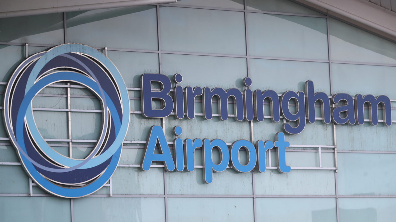 The outside of Birmingham Airport. The word Birmingham in in dark blue whereas the word airport is in a light blue. There is a circular dark and light blue logo next to the the words.