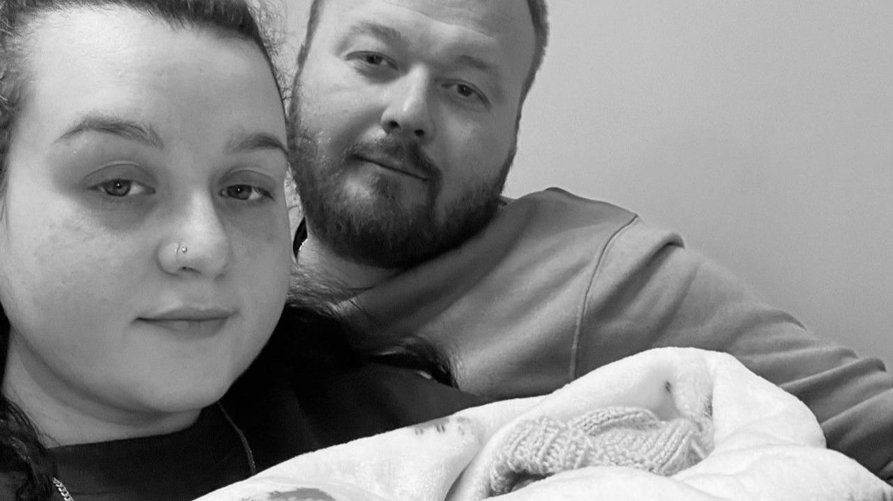 Zoe Wilbourne and Matilda's father, George Jefferies in hospital, holding a baby. You can only see a baby's knitted hat and swaddling.