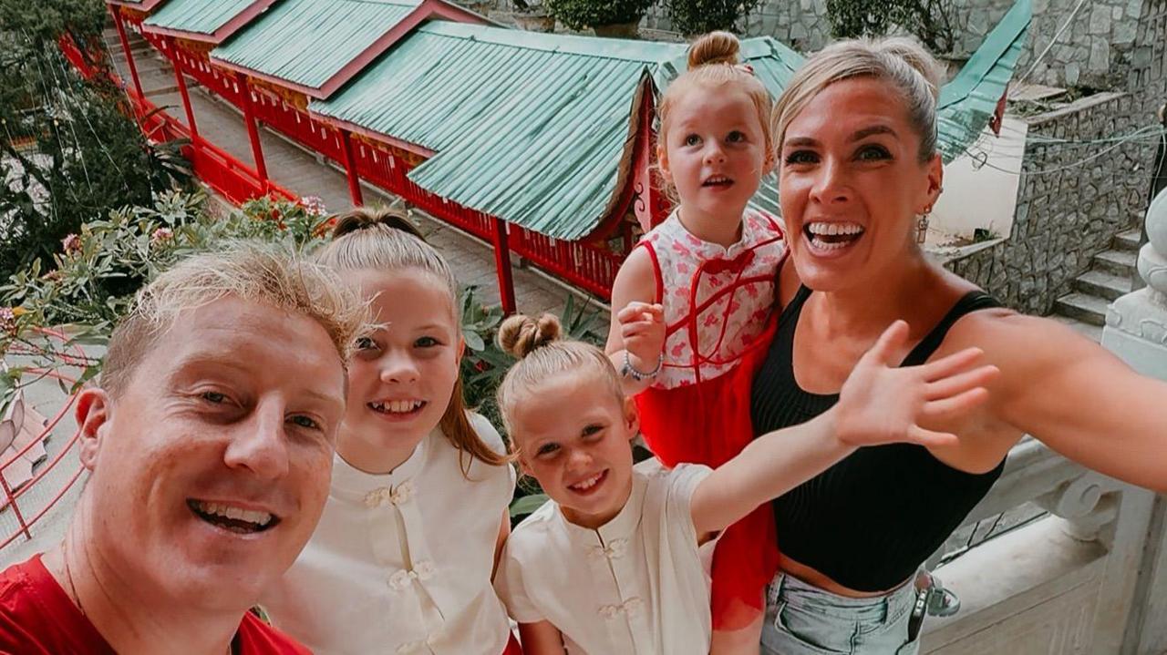 The family smiling at the camera, the children are wearing traditional Chinese dress