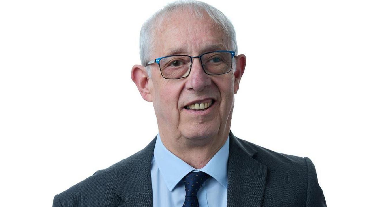 Councillor Les Shaw, a gentleman wearing glasses and a navy suit with light blue shirt.