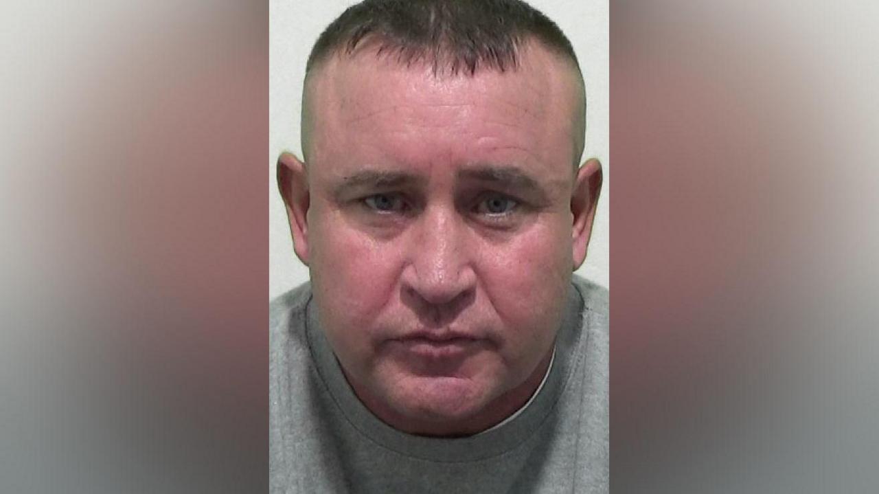 Mugshot of a man with short dark hair and a flushed face.