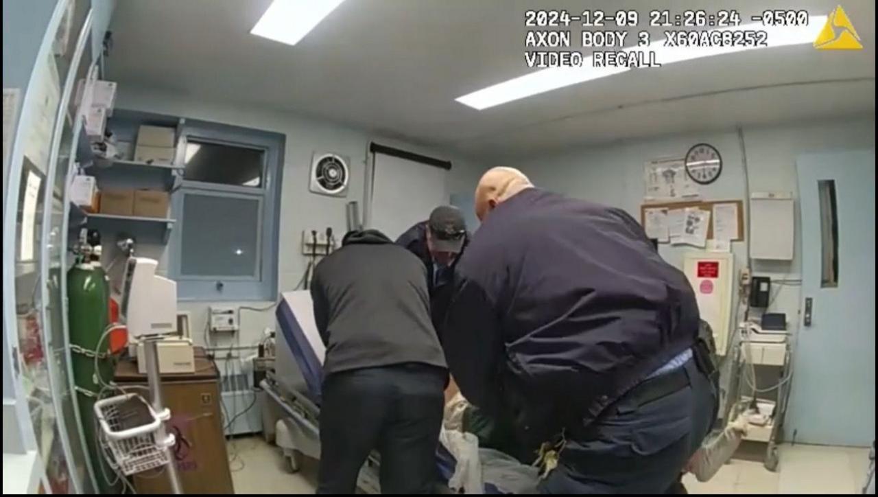 A group of men huddled around an examination table in a medical office, it is apparent that someone, barely visible, is on the table itself