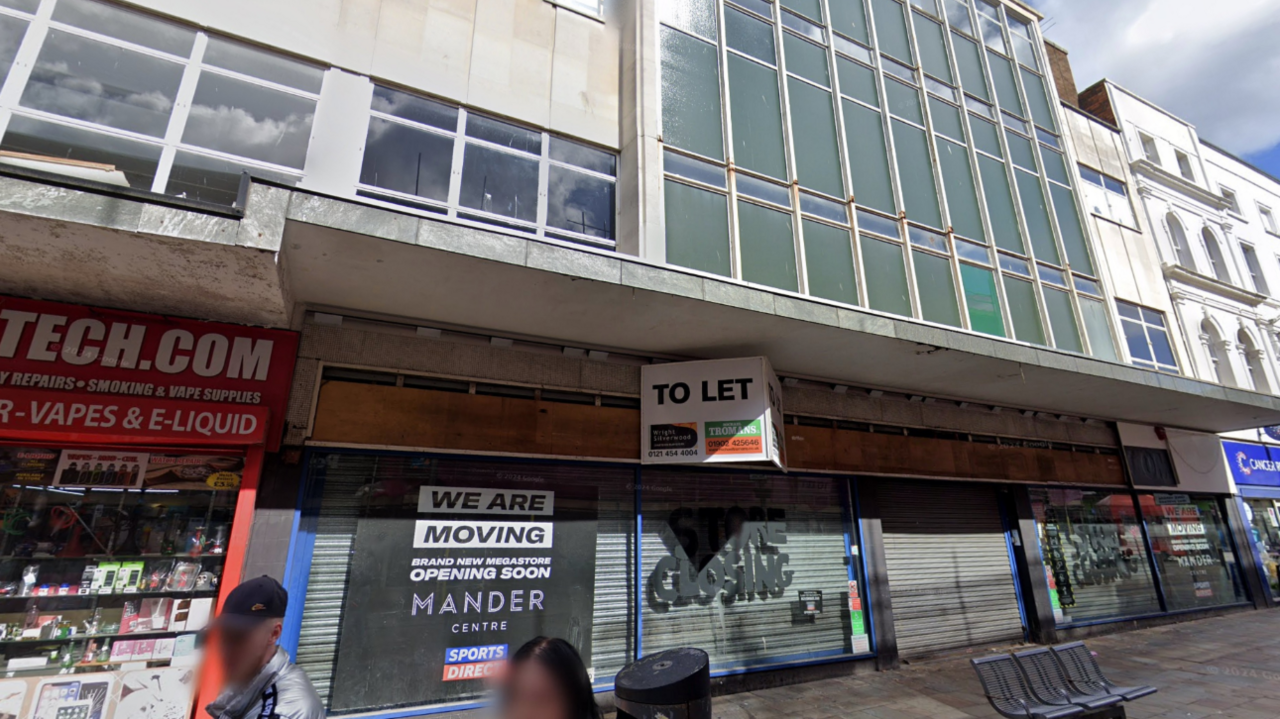 The front of a four-storey building, with shutters behind the ground floor windows and a large to let sign above.