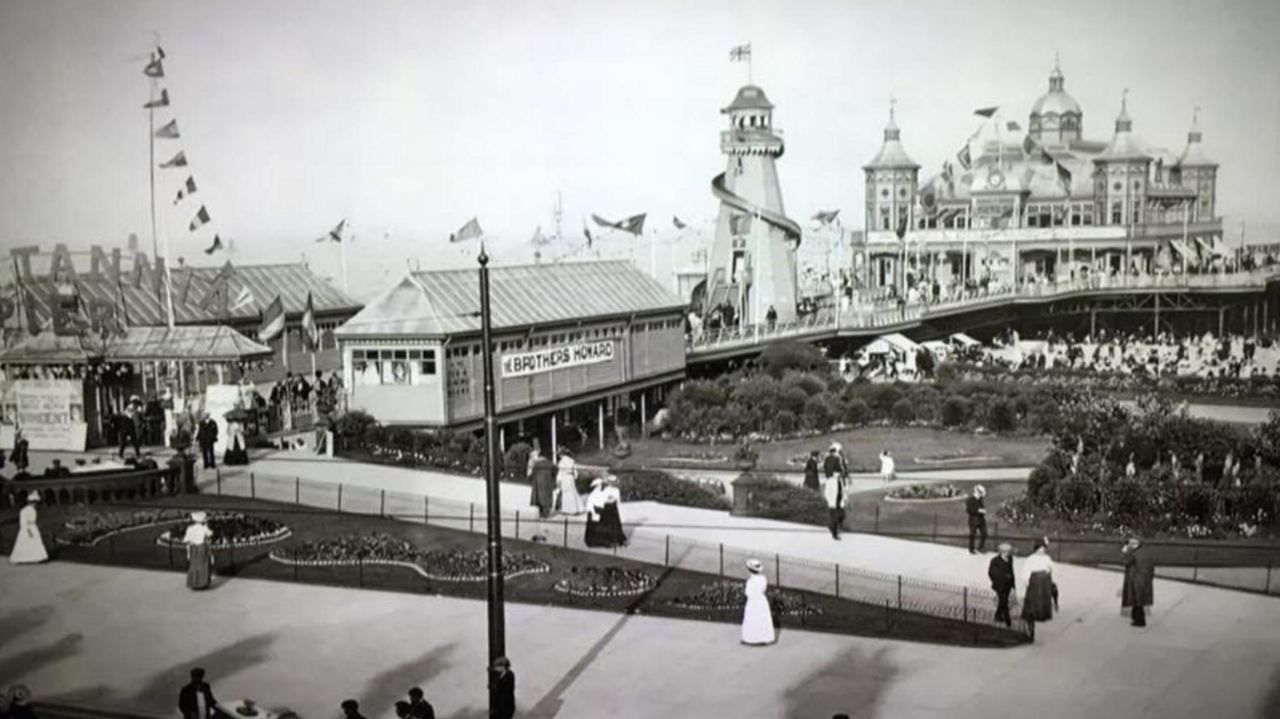 Old black and white photo of Great Yarmouth Britannia Pier, showing a buzz of activity including a helter skelter, the pier building and hundreds of people enjoying the sun