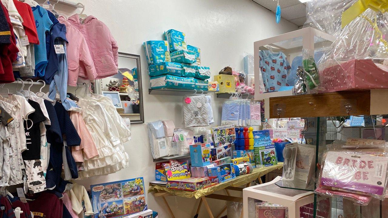 The inside of the shop has stacks of nappies on shelves, clothes hanging on rails and boxes of toys stacked on a table. 