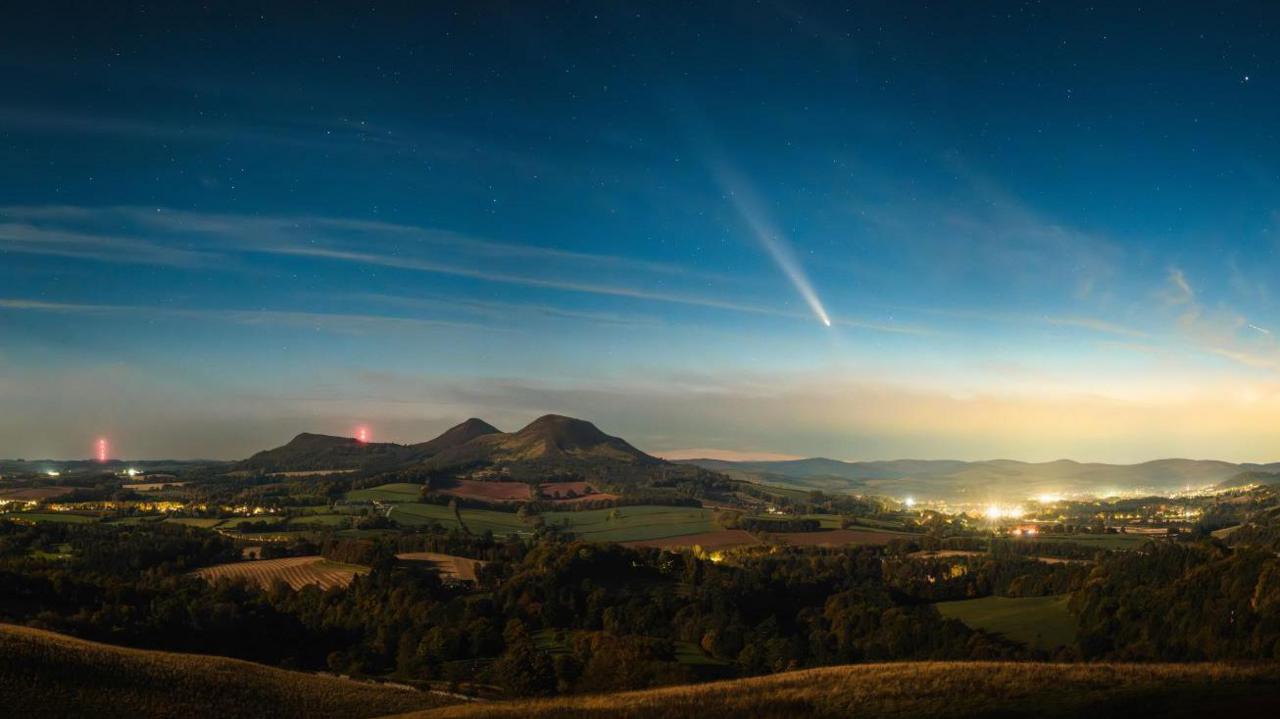 Comet A3 pictured over hills and a settlement with streetlights.