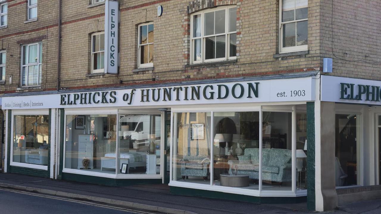 The shop as it is today. It has a white store front and big windows. The store name is printed in large green letters. 