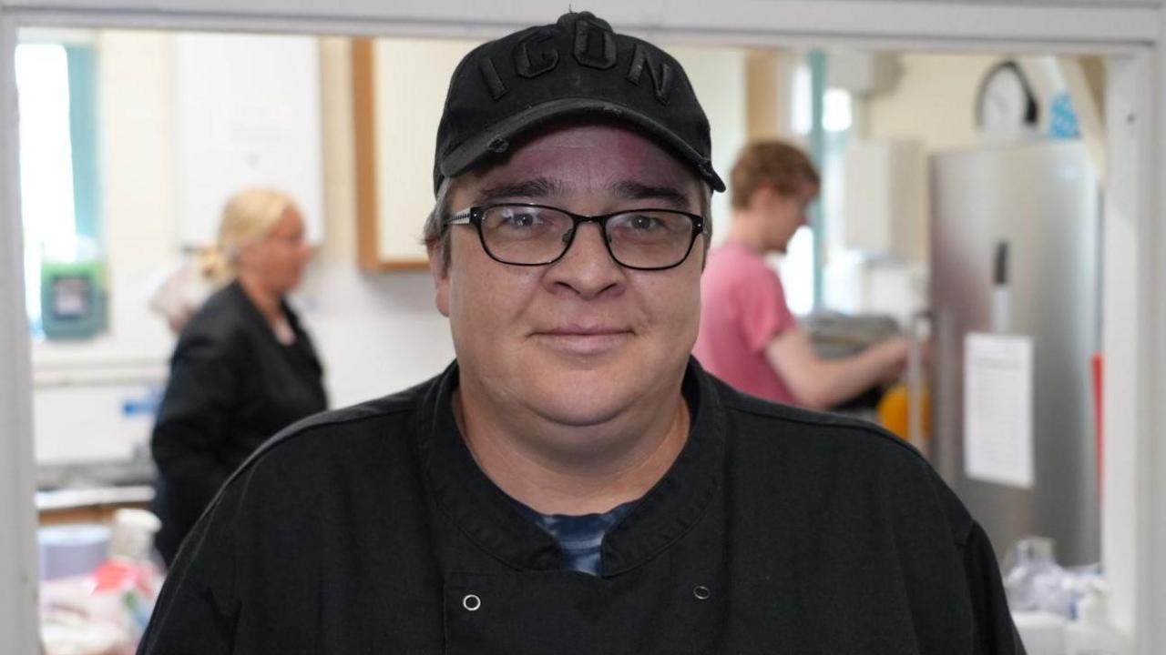 Lottie Eaton wearing black rimmed glasses, a black apron and black baseball cap.