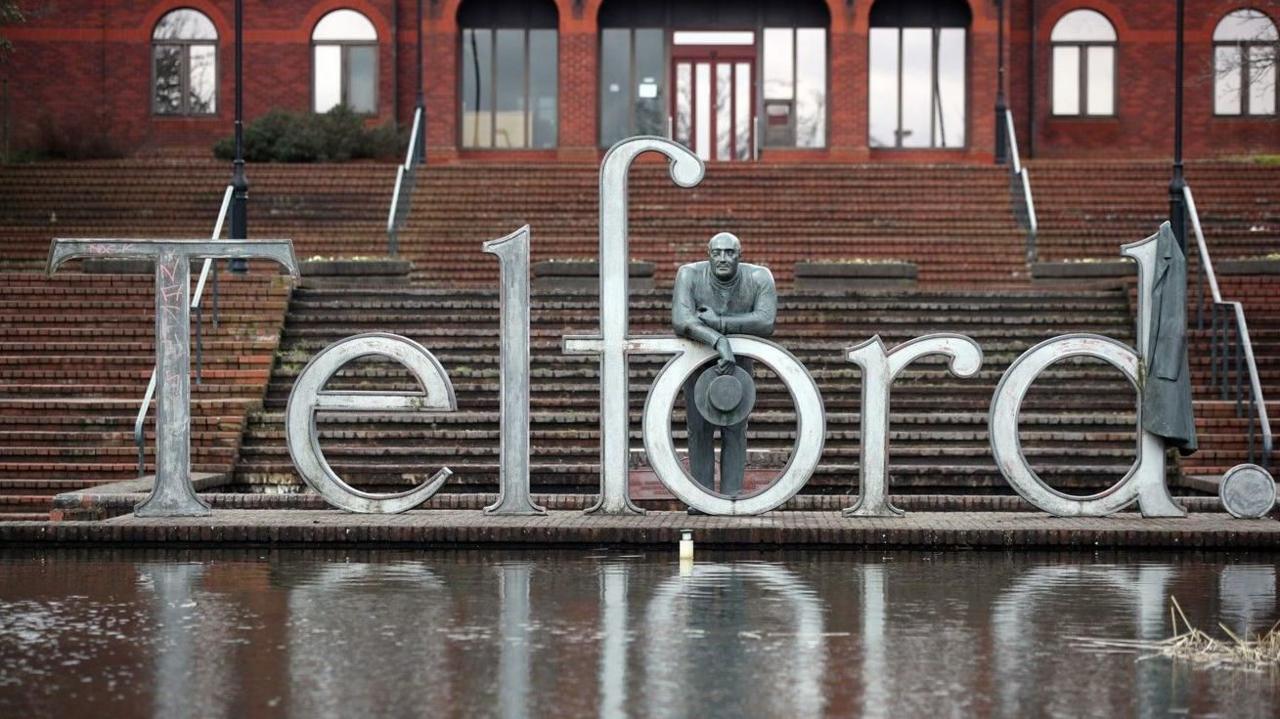 The art installation on Telford Square, Telford, made up of large metal letters spelling out the name of the town. A statue of Thomas Telford is leaning over the 'o', holding his hat. His coat is hanging on the 'd'.