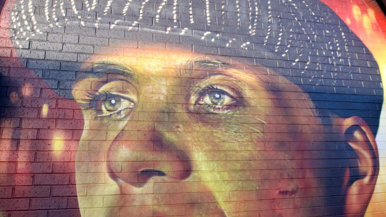 A close-up of the Thomas Shelby mural which has a red and orange background. Thomas is wearing a black flat-cap and has short brown hair.