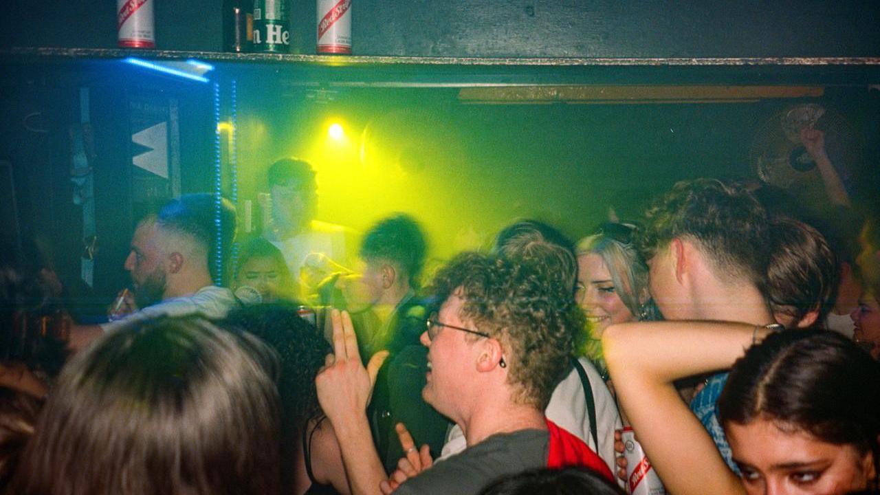 Clubbers packed into a dark venue partially illuminated with lime green lighting.