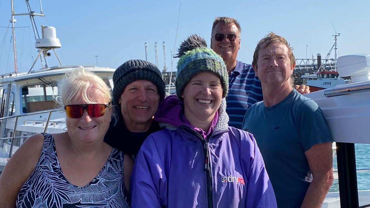 Marie-Helene Sanderson and her team are standing in a group and smiling at the camera. There are five of them and they are on a dock, with white boats in the background. Marie-Helene stands in the middle wearing a green woolly hat and a purple jacket.
