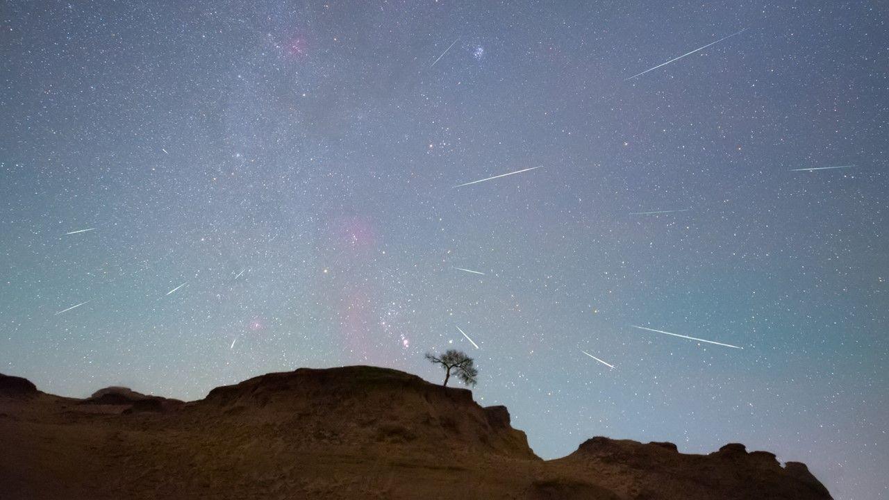 Meteors streak across a blue/pink sky above a hill