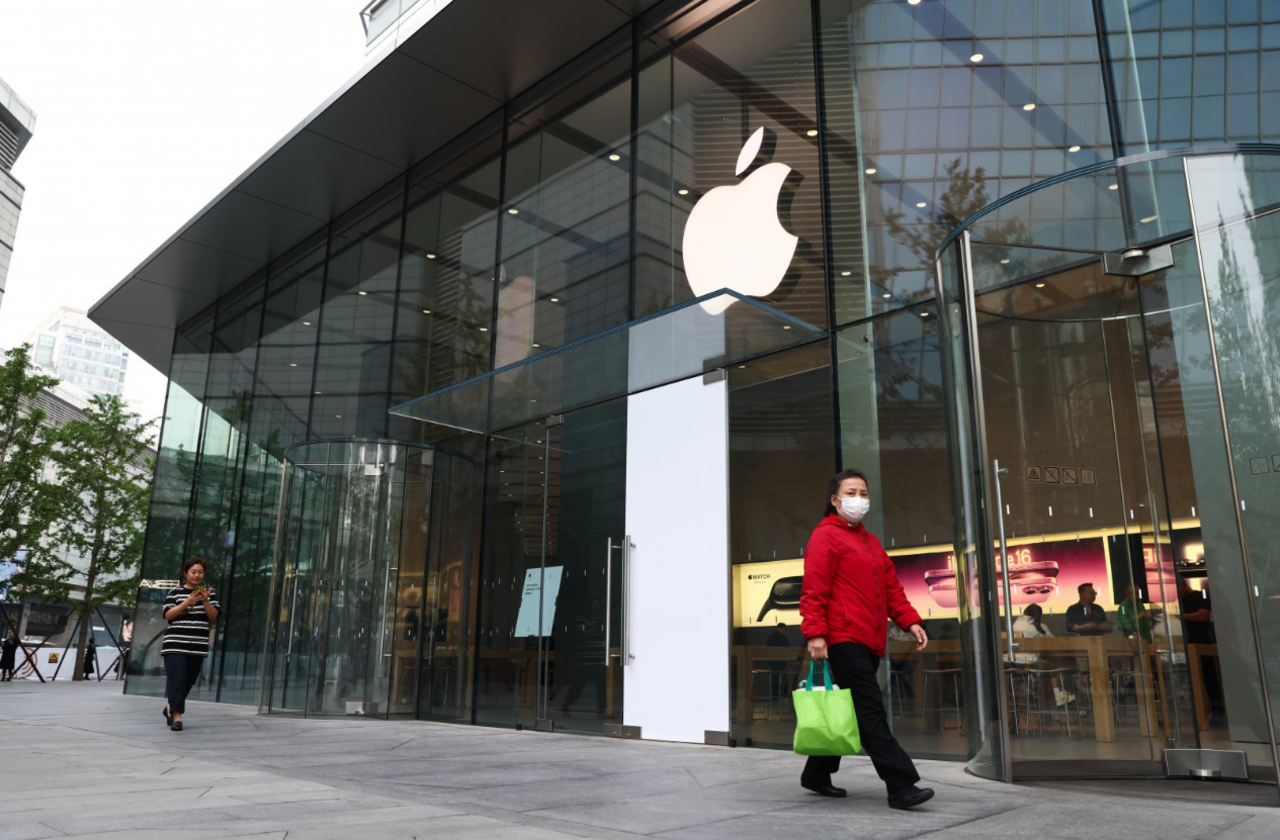 Woman wearing a red jacket and mask walks past an Apple store in Beijing on 12/5/2025