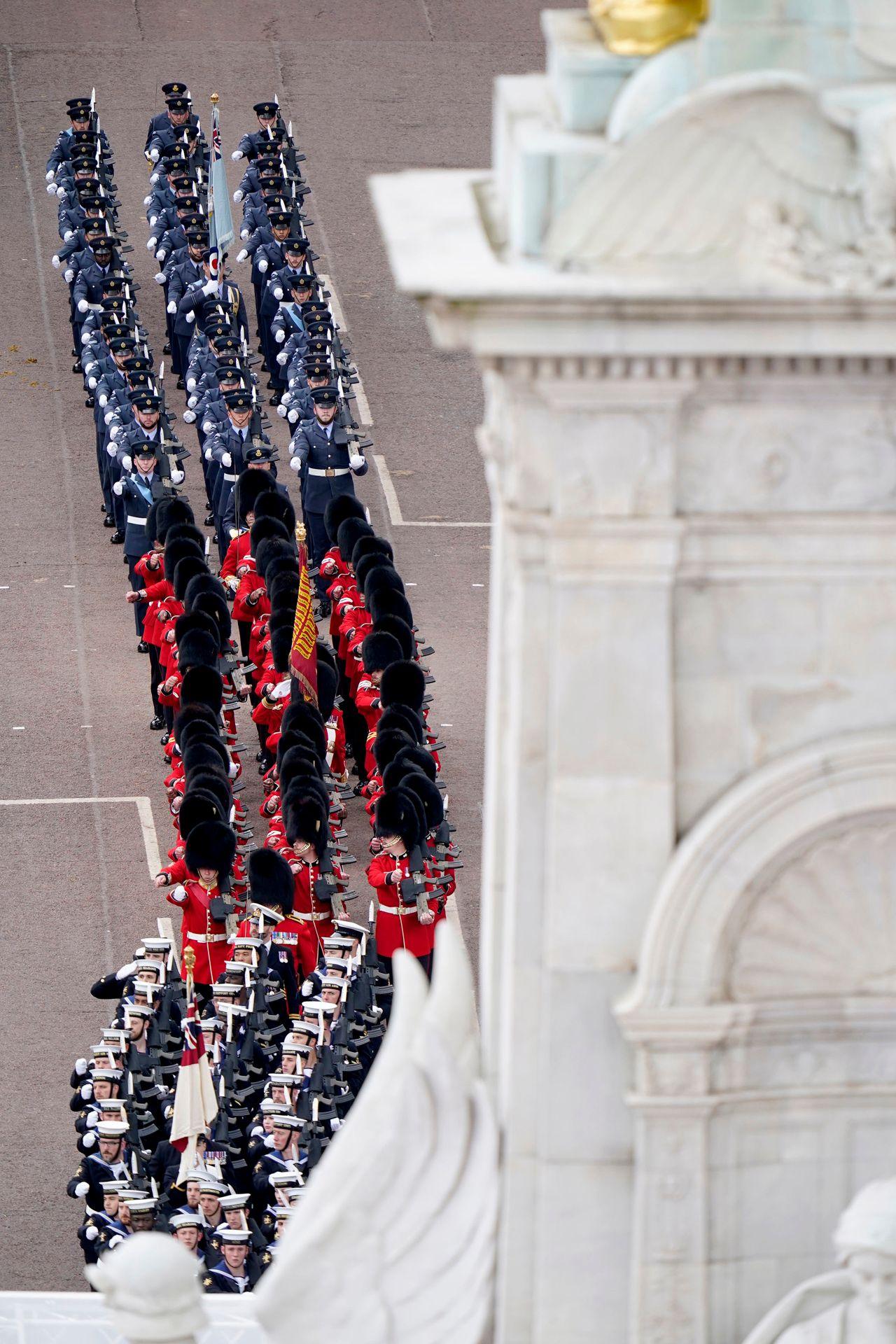 A narrow aerial view shows various groups of military parading down the Mall with the statue in front of Buckingham Palace in the foreground.