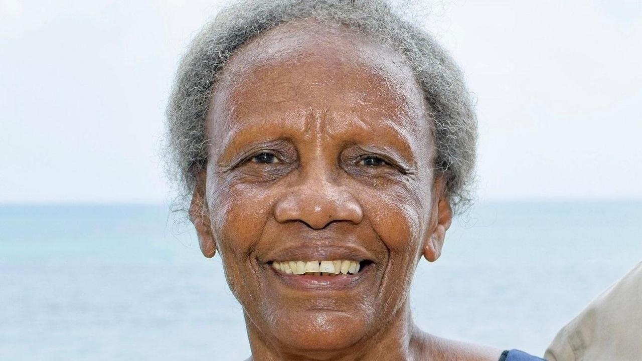A woman with grey hair looking at the camera smiling. The sky and sea are in the background.