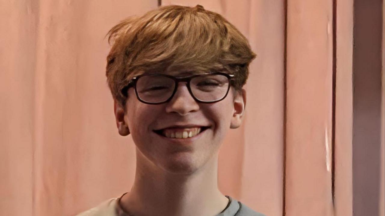 A headshot of Cyrus Perry, smiling at the camera, with dark glasses and brown hair