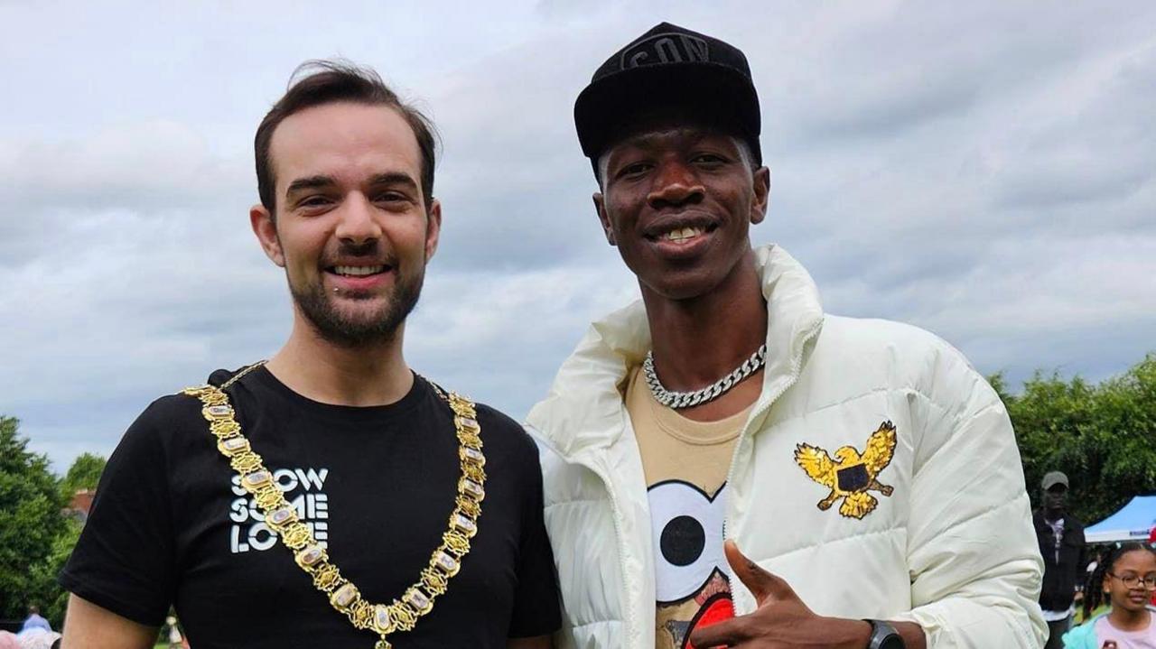 Zambian rapper Smack Jay wearing a white jacket and black baseball cap stands alongside the Lord Mayor Micky Murray wearing a black t-shirt.