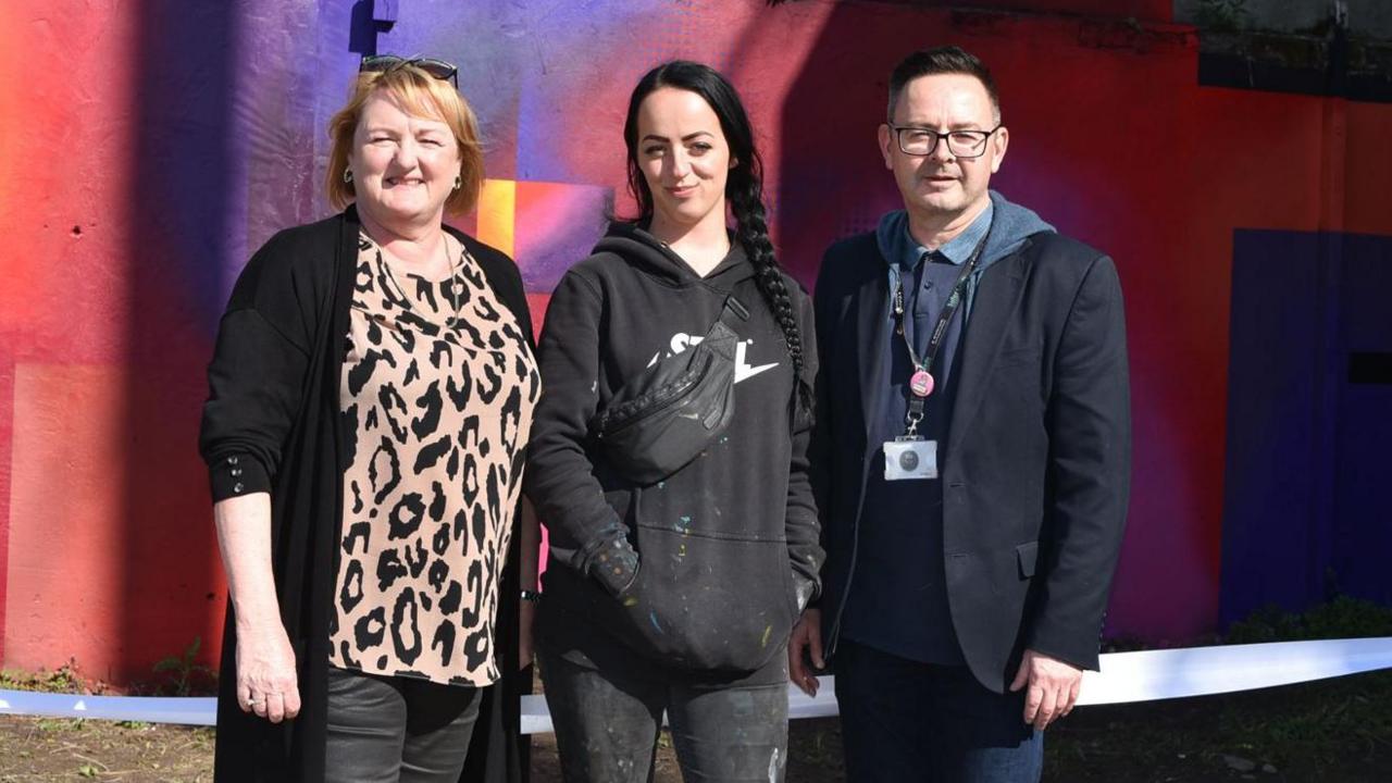 Councillor Debra Coupar, artist Harriet Wood and Simon Hodgson, head of Safer Leeds, standing in front of the mural