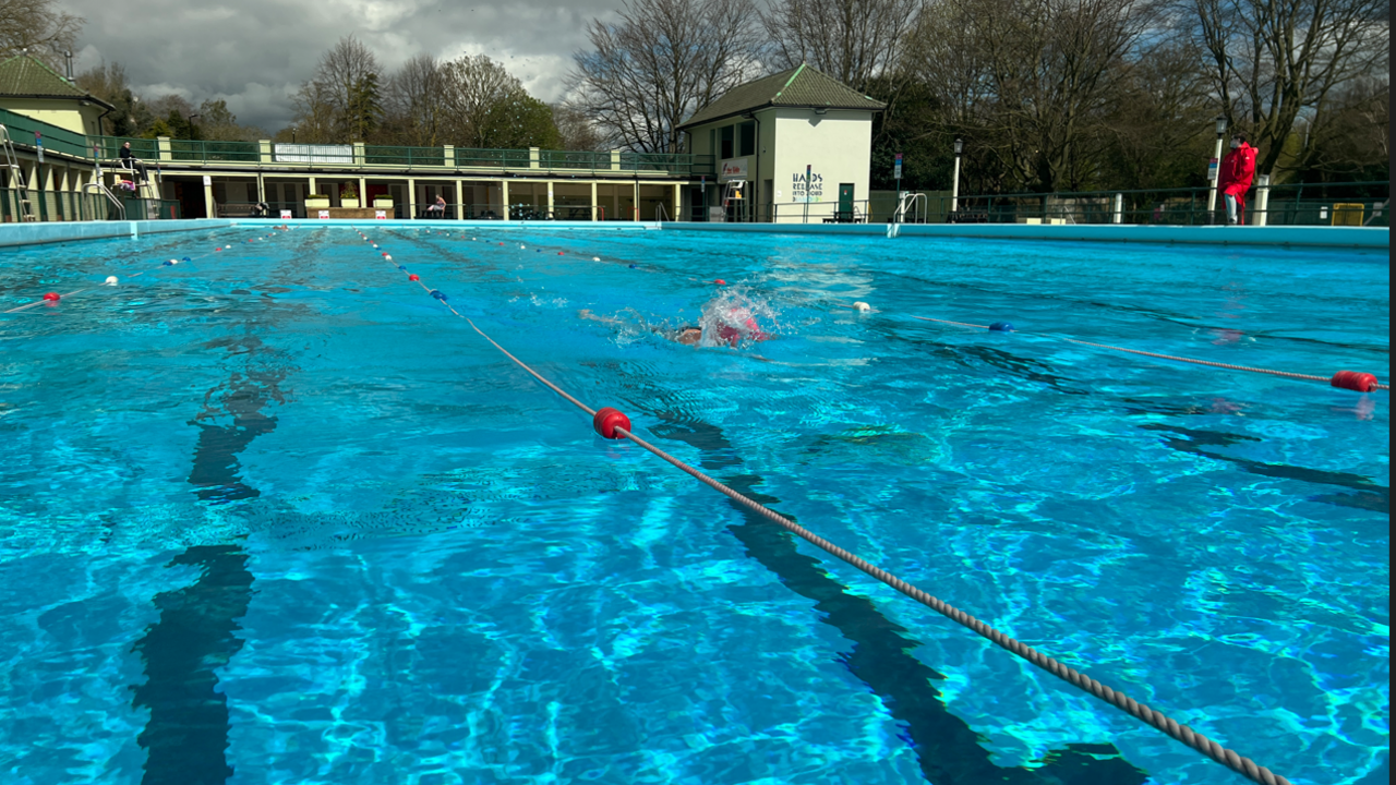 Outdoor swimming pool with lanes roped off and one person swimming.