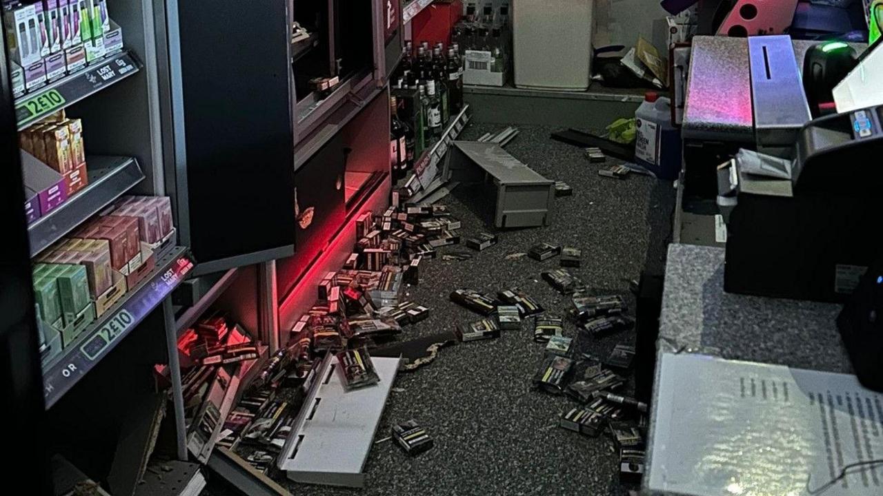 Packets of cigarettes are visible discarded on the floor of a shop, behind the till.