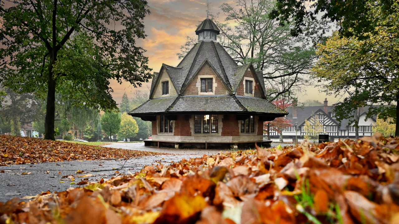 A hexagonal building with a triangular roof in the middle of a park with red autumn leaves all around