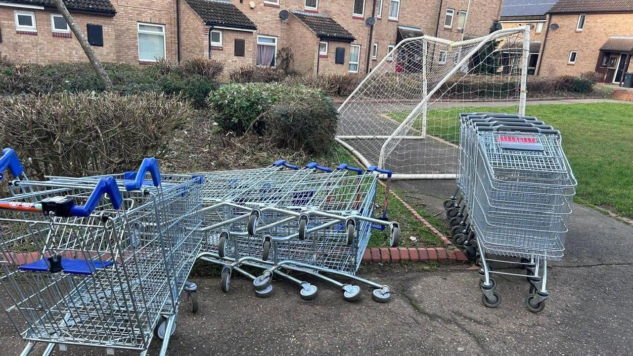 Metal trolleys collected and lined up. Some have fallen on the ground in front of a row of houses.